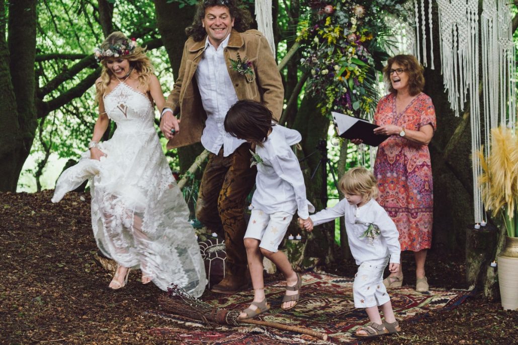 unforgettable wedding ceremony as the bride and groom, holding hands with their sons jump over the broom, in a celebrant ceremony outside