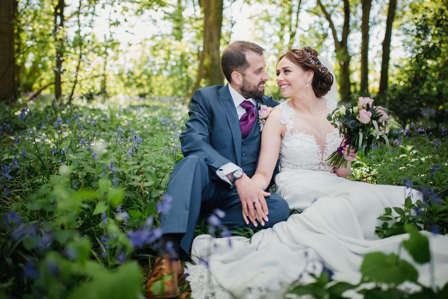 Traditionally dressed bride and groom are sat in a beautiful woodland with flowers surrounding them