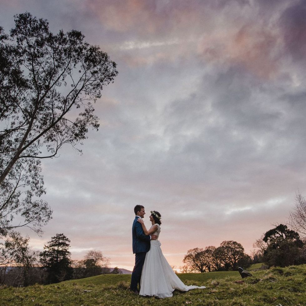 at their Valentine's Day wedding bride and groom  in distance beneath atmospheric wintery sky that has hints of pink