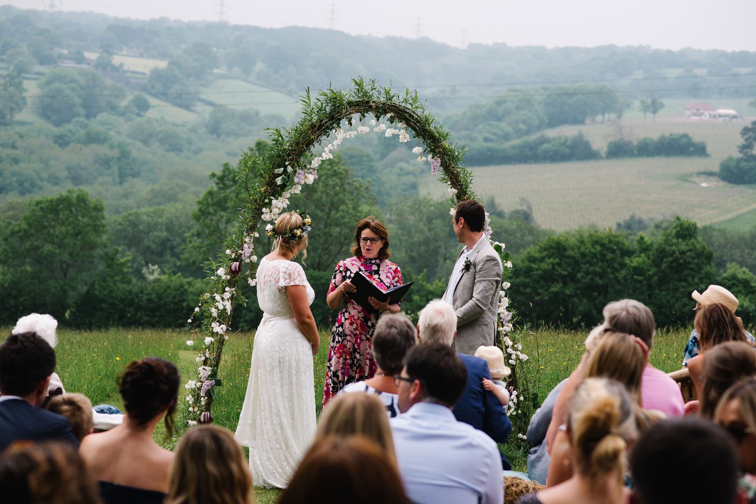 Registrars and Celebrants - her Celebrant Fan is leading a wedding ceremony in the countryside, the bride and groom stand before a floral arch