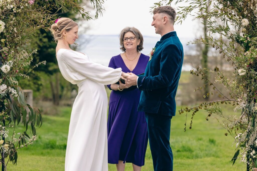 bride and groom at an outdoor ceremony celebrant wearing purple dress smiling telling their love story
