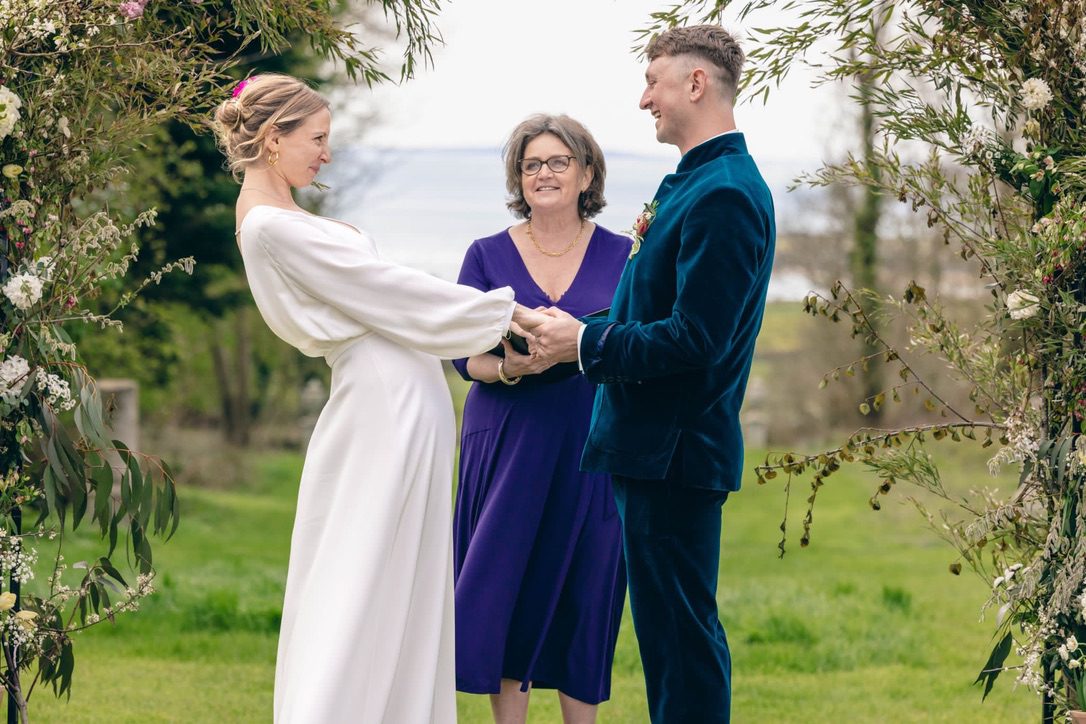 picture of bride and groom holding hands and wedding celebrant at a beautiful wedding venue, smedmore house with th sea in the background