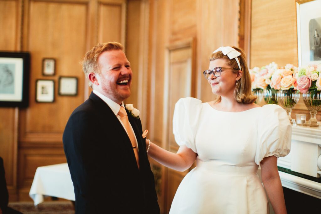 successful wedding planning a bride and groom laugh in a wood panelled room