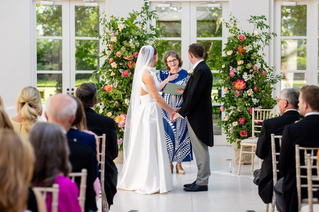 unforgettable wedding ceremony in an orangery where the bride and groom hold hands in front of celebrant Fan.