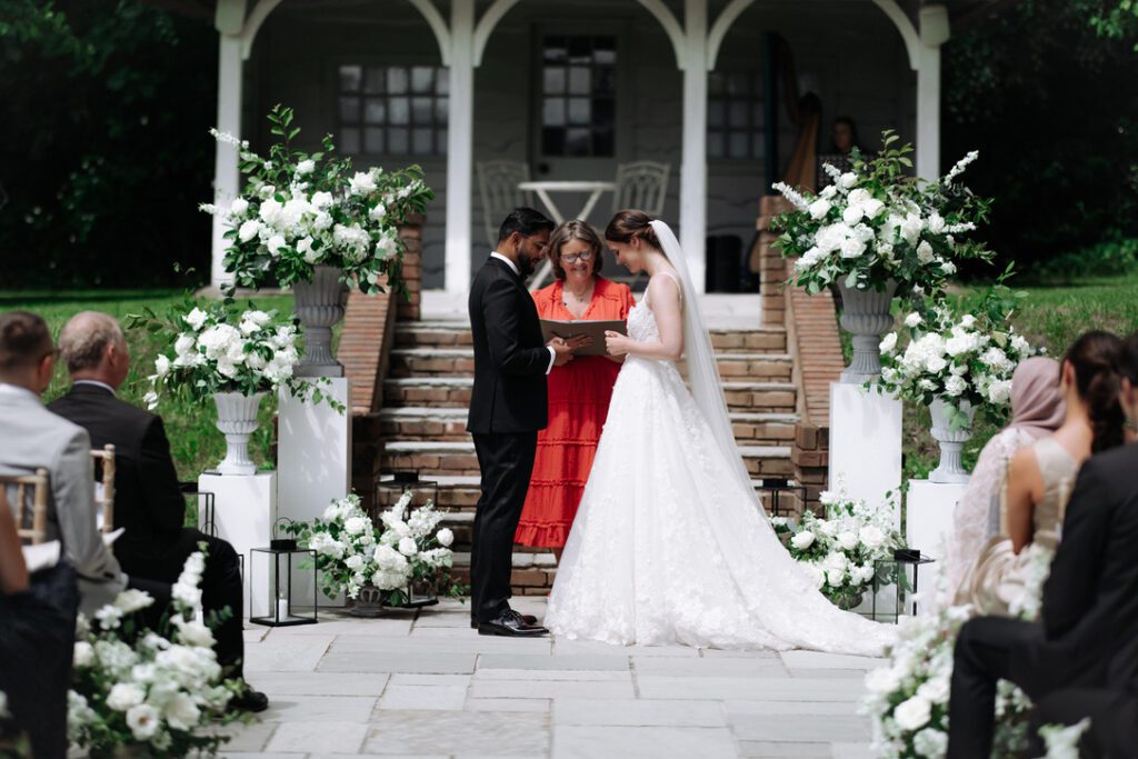 Celebrant for your wedding? couple standing with celebrant Fan in red dress at foot of steps between 2 urns filled with flowers at Deer Park