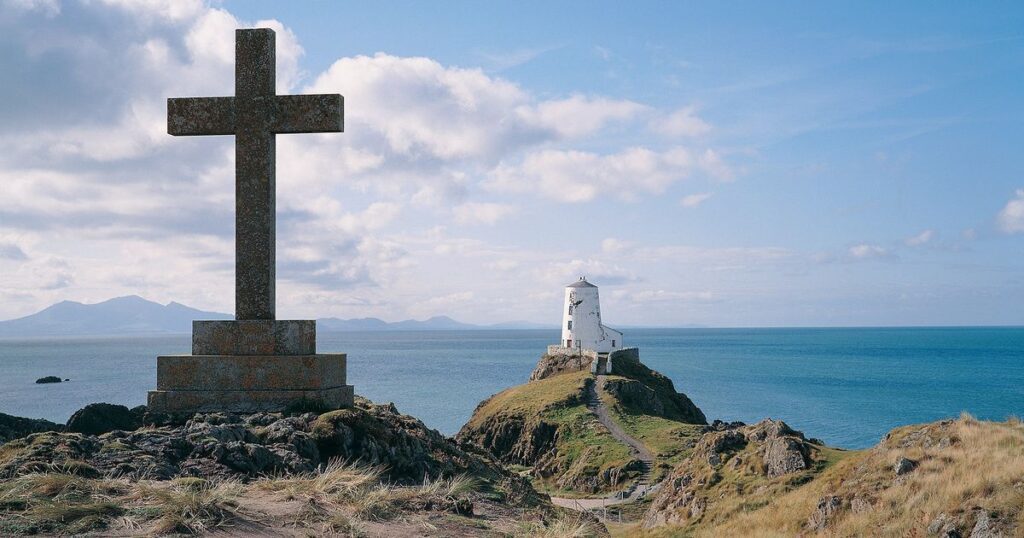 a picture of the supposed burial place of St Dwywen showing a cross and lighthouse with sea behind