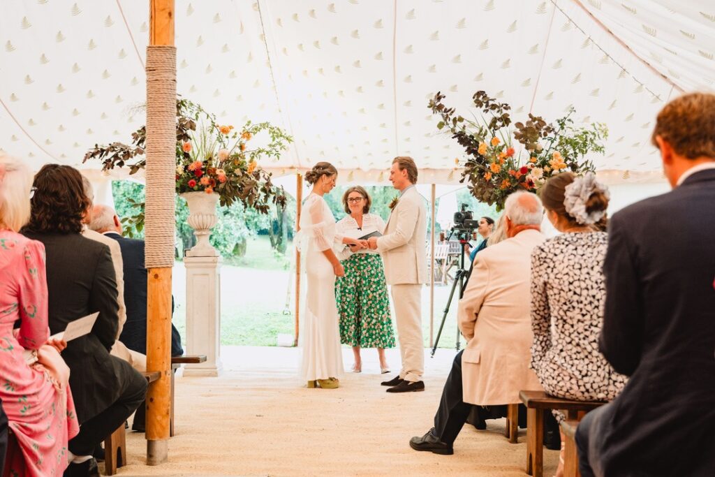 wedding at home - Oscar and Charlotte exchange vows in the marquee while guests watch on sat on benches