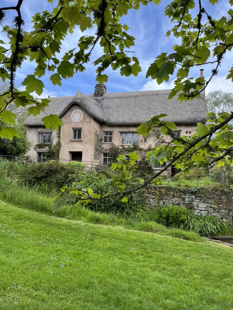 Hayne Devon a beautiful wedding venue with a sightly pink coloured brick and thatched roof with a glimpse of the magical garden in the foreground