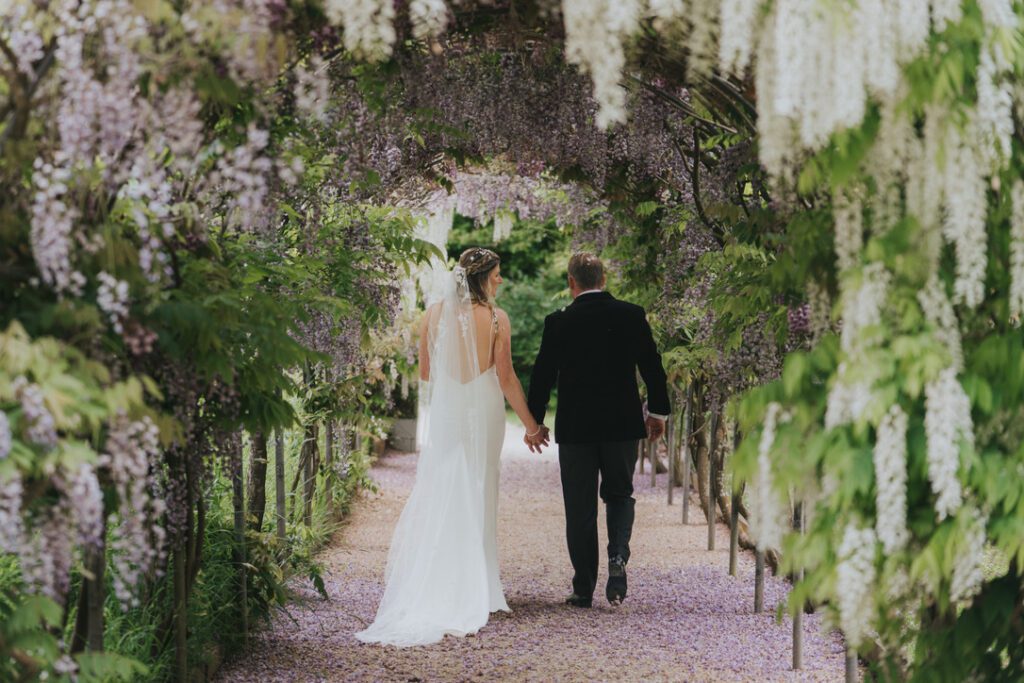 bride and groom walking through wisteria tunnel in full bloom at Deer Park Country House