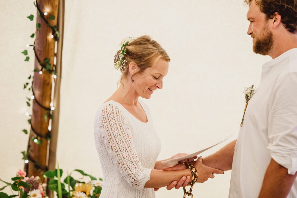 a bride reading her vows with cords around hers and her husbands wrists having completed a handfasting ceremony 
