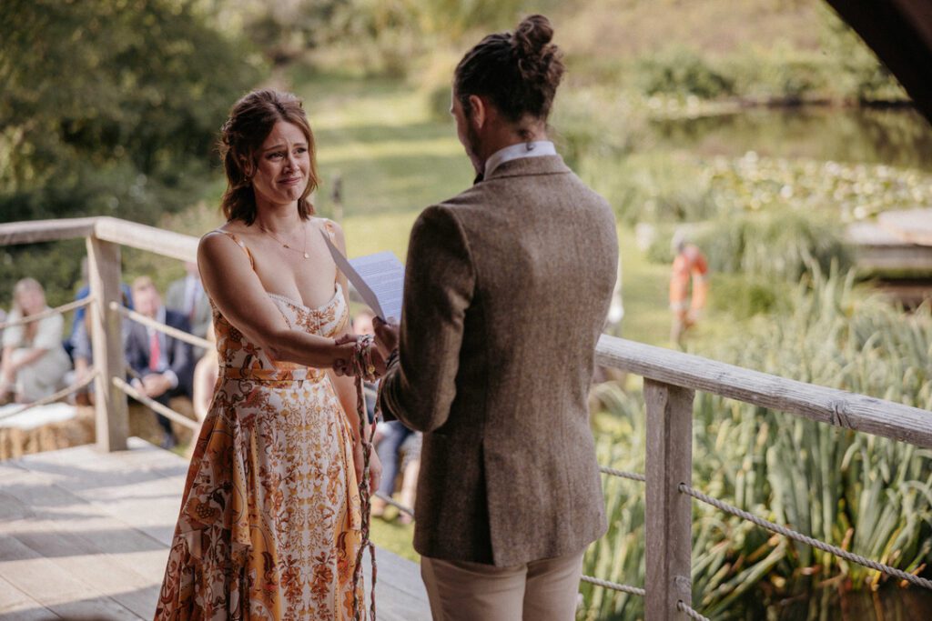 emotional bride in rust and cream wedding dress facing her groom his back to camera with their hands tied for a hand  fasting ceremony 
