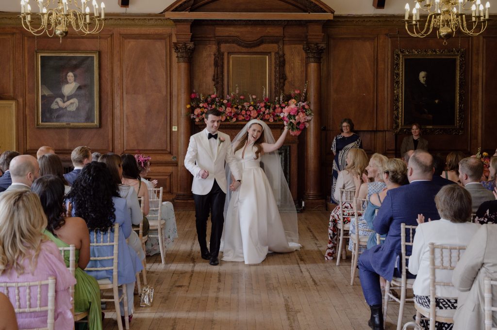 bride and groom celebrating after their marriage groom in tuxedo and bride with arm raised and bouquet in air