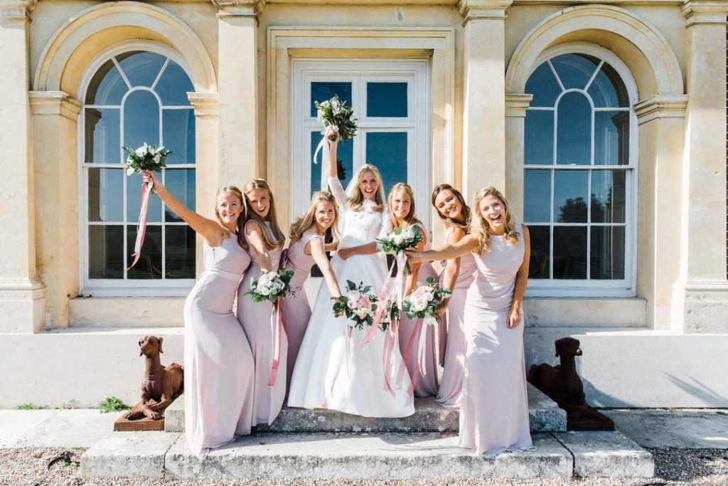bride and bridesmaids standing on steps of grand house with arched windows 