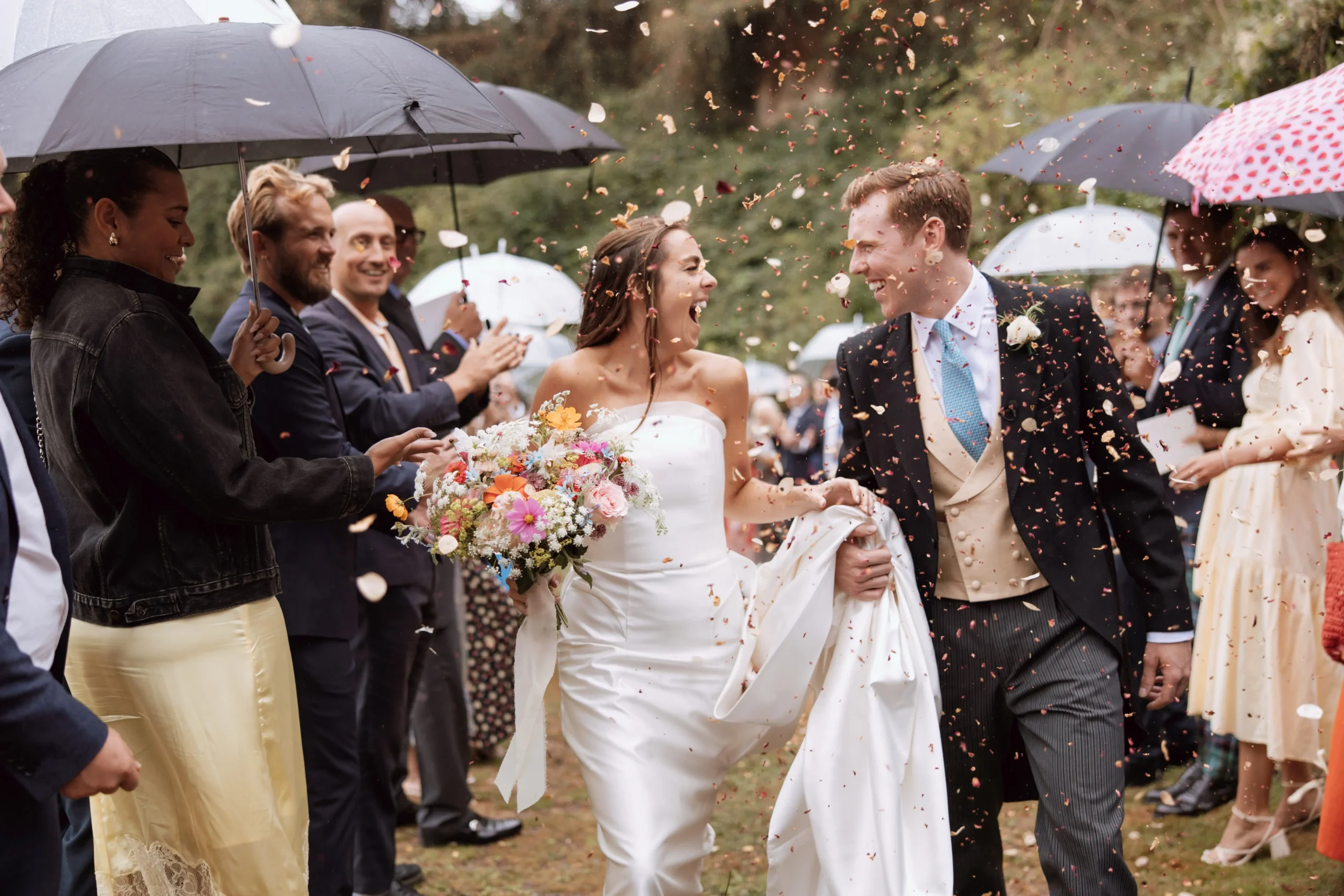 J & J walking through confetti A bride and groom enjoying the experience of walking through their guest (holding umbrellas) as they shower them in confetti