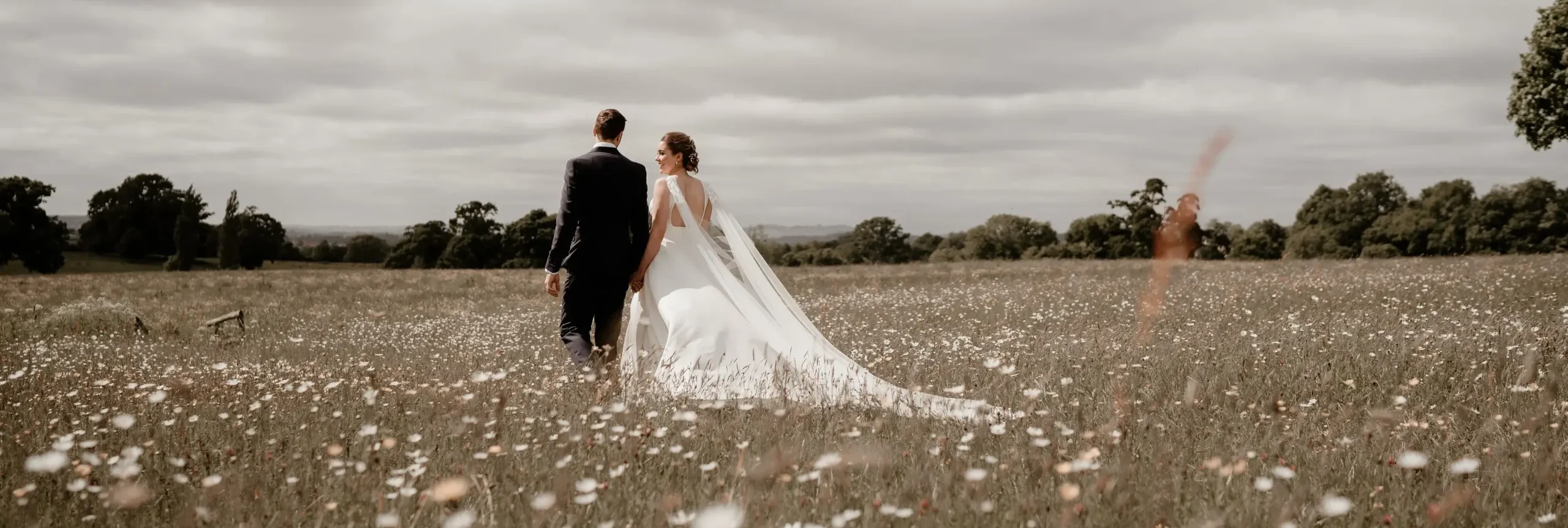 A bride and groom walking through a flower meadow on a cloudy day
