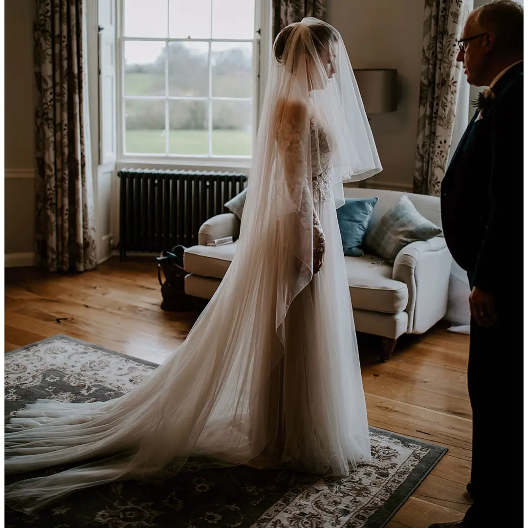 A bride in her bedroom with her Dad A bride stands in a bedroom , a veil covering her face, her father stands opposite her