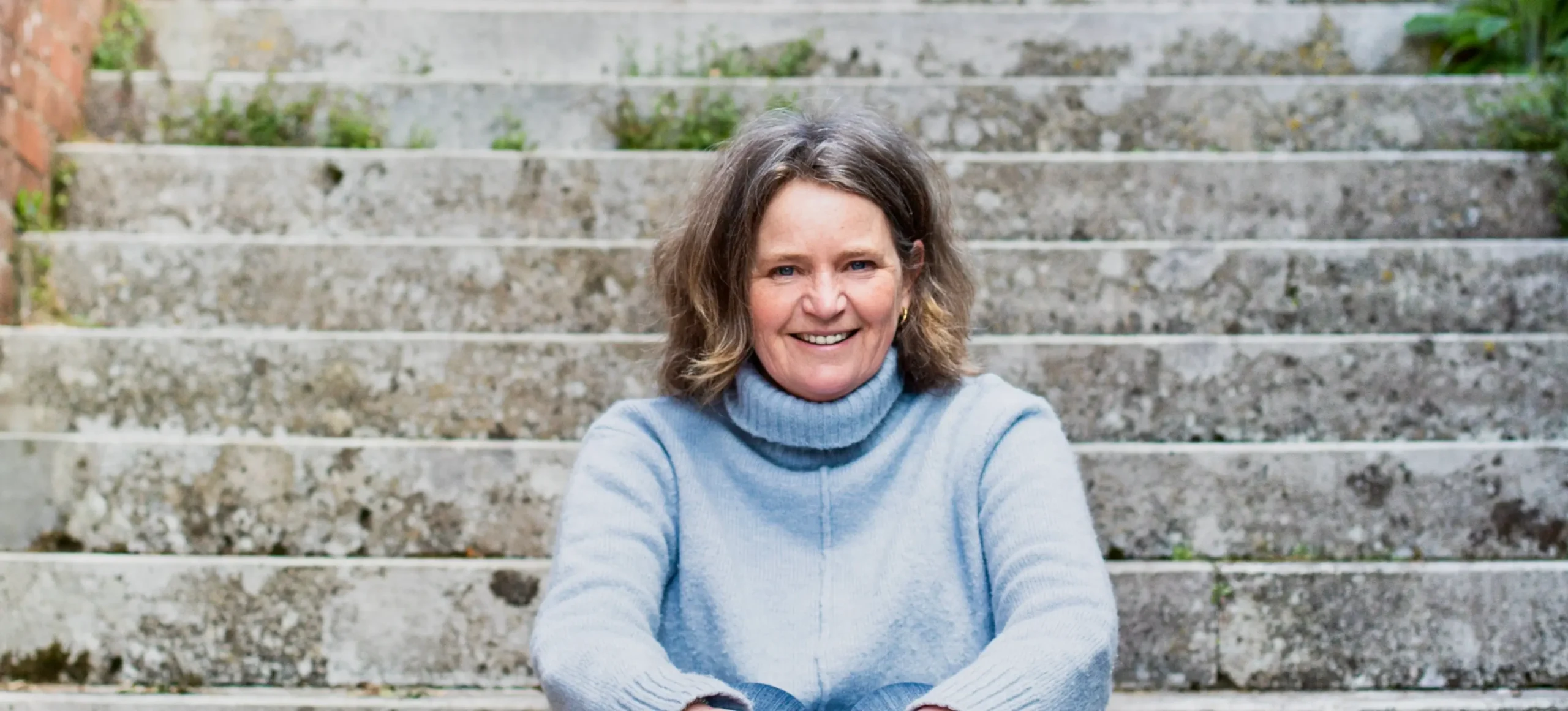 English wedding celebrant Fan in a blue jumper sat on stone steps